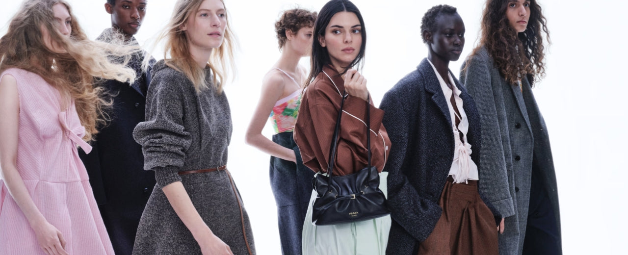 Prada luxury fashion banner showcasing diverse models in refined, contemporary silhouettes, highlighting the brand’s minimalist design, modern tailoring, and iconic Italian luxury aesthetic.