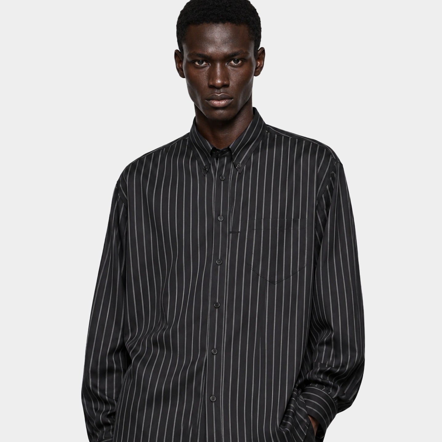 Editorial model wearing an oversized black pinstripe button-down designer shirt from ELLIS ROSCH against a white background.