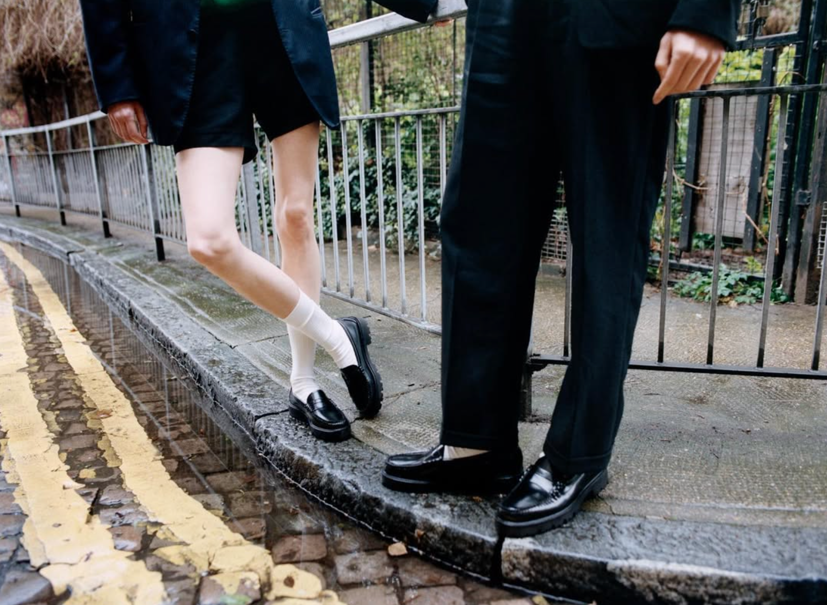 Two people wearing black G.H. Bass Weejun loafers — one styled with shorts and white socks, the other with tailored trousers — capturing the loafer’s evolution from prep-school uniform to cultural statement.