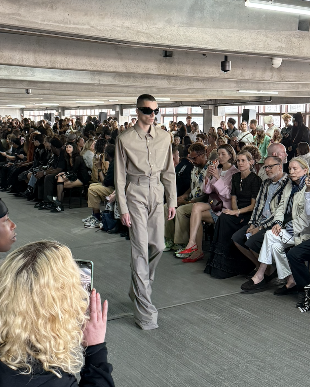 Han Kjøbenhavn runway — model in monochrome beige tailored shirt and wide-leg trousers, styled with futuristic sunglasses, showcasing Scandinavian minimalism with an avant-garde edge.