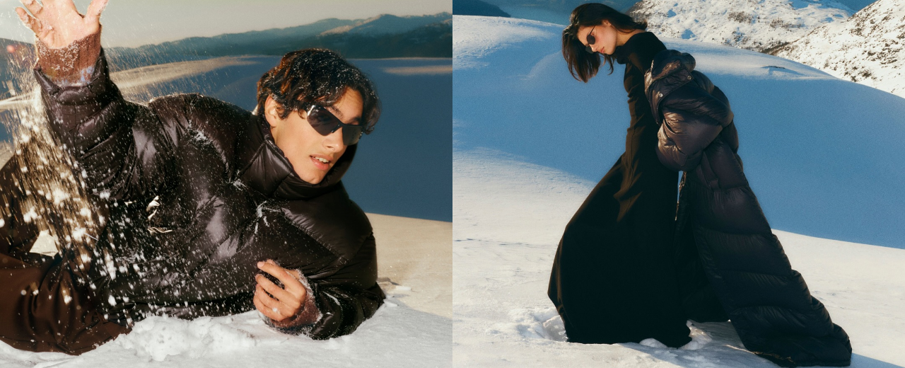 Fashion editorial of two models in a snowy mountain landscape wearing glossy black puffer jackets and sleek winter outfits, showcasing contemporary designer outerwear for ELLIS ROSCH.