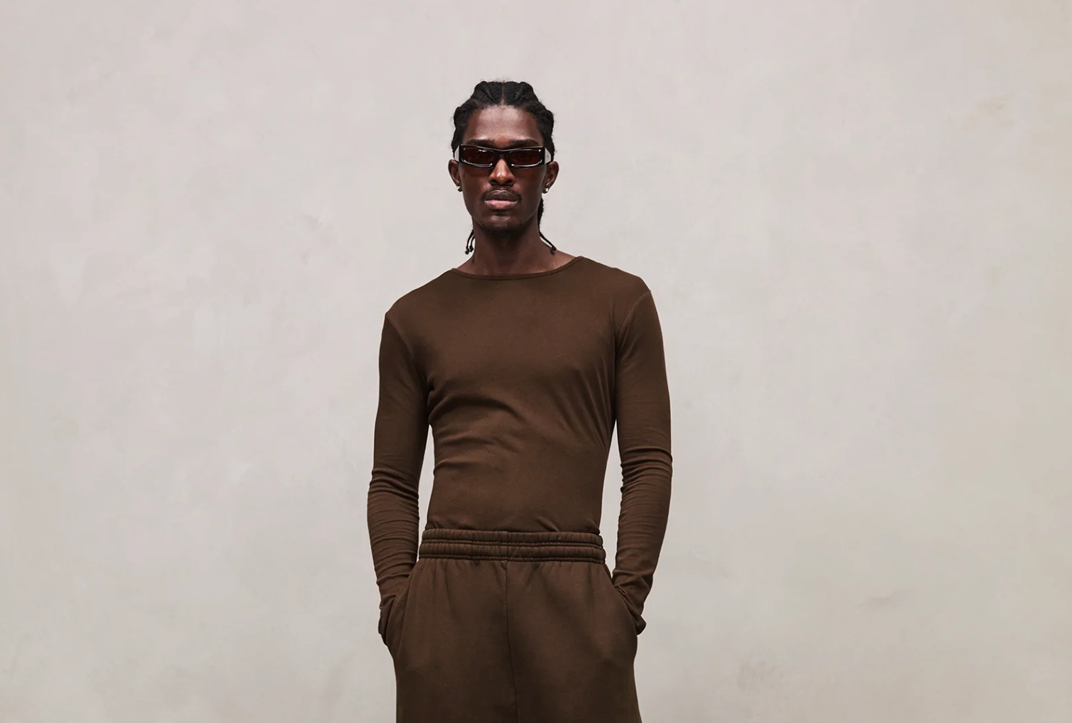 Entire Studios look — model in monochrome brown long-sleeve top and relaxed trousers, styled with futuristic sunglasses, embodying minimalist streetwear with utilitarian edge.