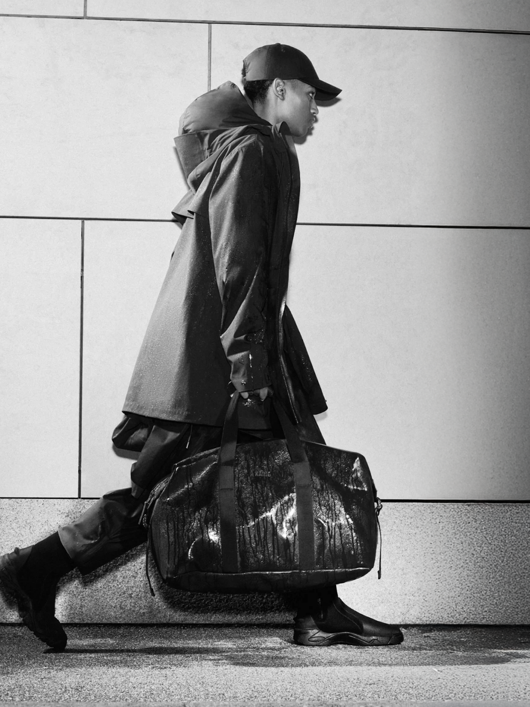 RAINS black waterproof duffel bag styled with raincoat, cap, and boots — Scandinavian rainwear designed for urban movement and functional fashion.