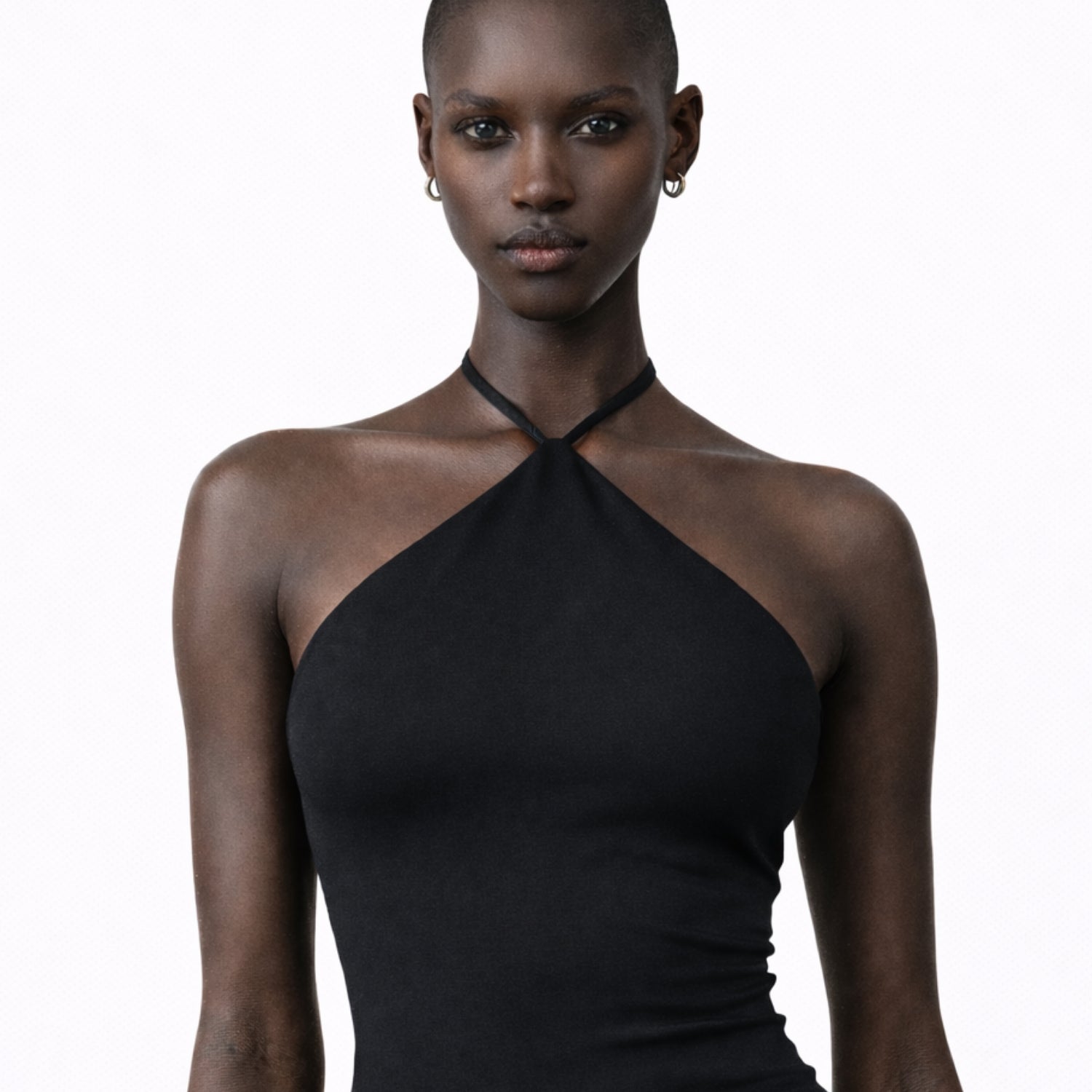 Female model wearing a black Jacquemus halter bodysuit from ELLIS ROSCH Women’s New Arrivals, styled with a minimal, sculpted silhouette. The top features a high neckline with thin straps that wrap around the neck, creating a clean, open shoulder line and a sleek, form-fitting shape. Shot against a neutral studio background, the image emphasizes the garment’s smooth texture, precise tailoring, and modern elegance. The look reflects Jacquemus’ signature approach to refined minimalism—sensual, architectural, 